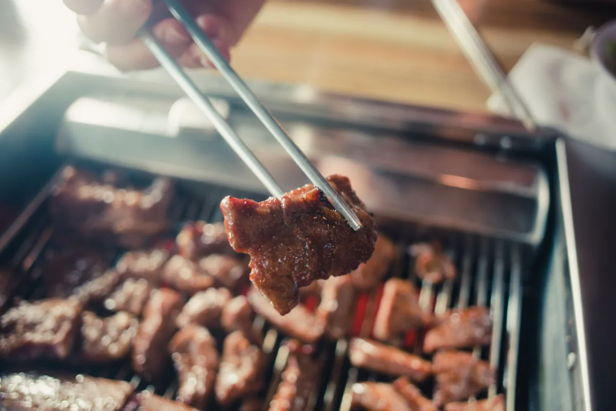 卓上グリルの上で金属の箸でつまんだ焼肉